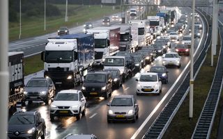 Auto’s met koplampen aan staan in drie rijen op de snelweg in de file bij regenachtig weer.