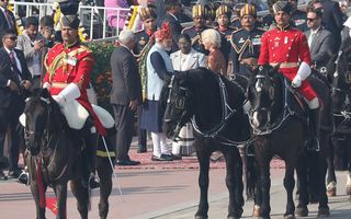 In het midden van de foto geven drie mannen en een vrouw elkaar de hand. Ze worden omringd door mannen in kleurrijke uniformen, van wie sommigen te paard.