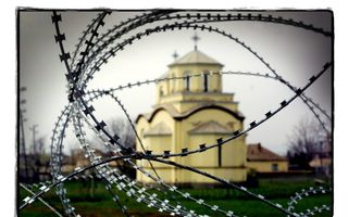 Foto van een zachtgeel kerkje met op de voorgrond prikkeldraad.
