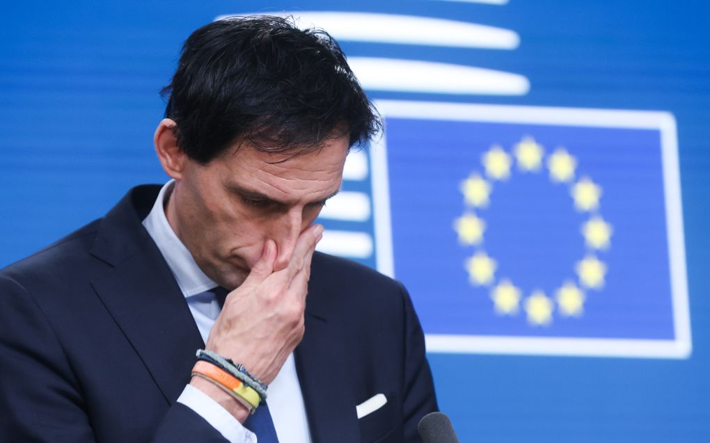 Wopke Hoekstra kijkt bedenkelijk voor een blauwe wand met daarop de Europese vlag.