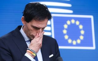 Wopke Hoekstra kijkt bedenkelijk voor een blauwe wand met daarop de Europese vlag.