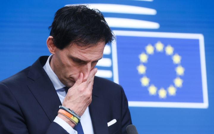 Wopke Hoekstra kijkt bedenkelijk voor een blauwe wand met daarop de Europese vlag.