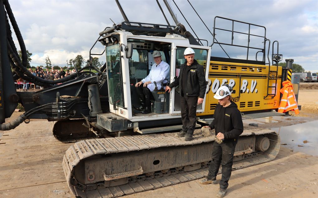 Ds. D. de Wit heeft vrijdagmiddag de eerste paal geslagen voor het nieuwe kerkgebouw van de gereformeerde gemeente in Kesteren. Nadat de predikant de heimachine had bediend, mediteerde hij kort naar aanleiding van Psalm 87. Ouderling C. van de Bijl, voorzitter van de bouwcommissie, lichtte het proces vanaf de eerste gesprekken in 2018 toe en bedankte verschillende personen, commissies en bedrijven voor de „goede samenwerking en saamhorigheid”. De kerk aan de N233 krijgt 1500 zitplaatsen, met een mogelijkheid tot uitbreiding naar 1750 op de galerij. Het is de bedoeling dat het werk begin 2026 klaar is. beeld gereformeerde gemeente Kesteren