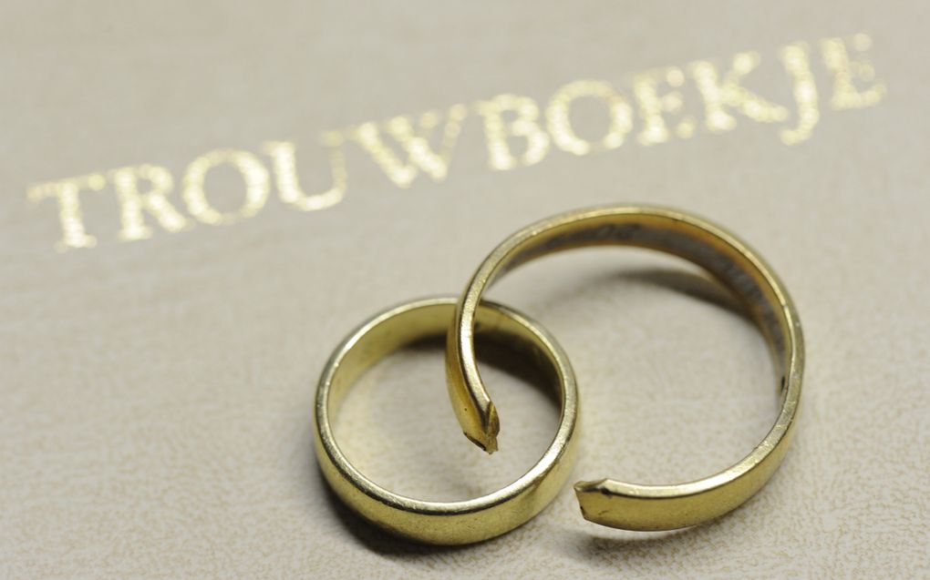Een gebroken en een ongebroken trouwring liggen op een trouwboekje.