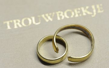 Een gebroken en een ongebroken trouwring liggen op een trouwboekje.