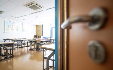 Doorkijkje in een klaslokaal. Op de muur hangt een wereldkaart. Diverse tafels en stoelen staan in de ruimte opgesteld.