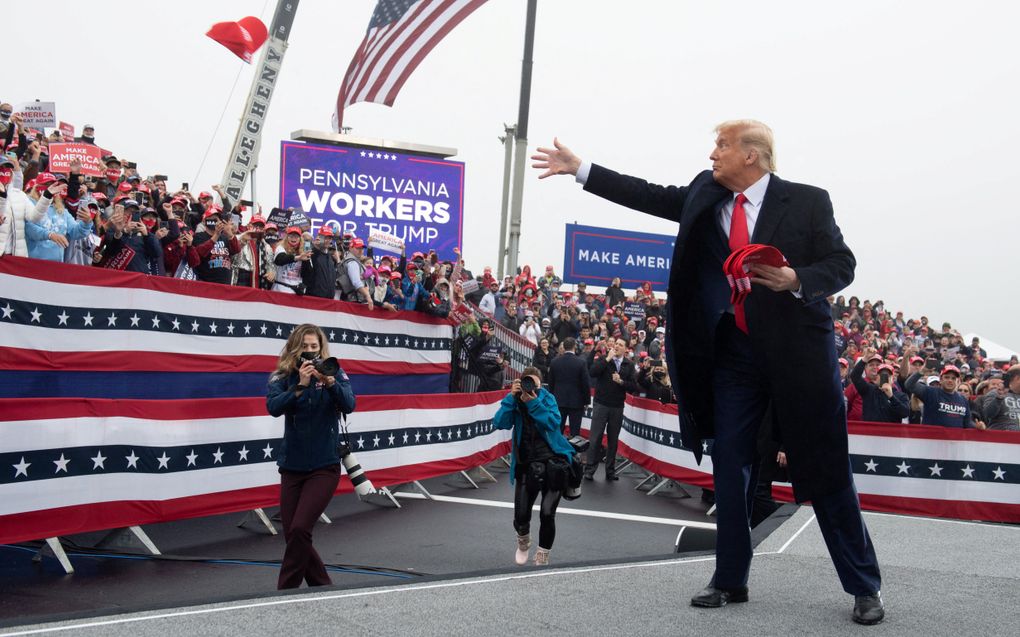 Foto van president Trump met een rode MAGA-pet op, tegen een blauwe lucht.