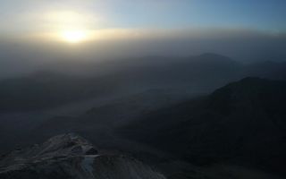 Het Sinaïgebergte, vrijwel duister, met in de nevels in de lucht de vroege ochtendzon.