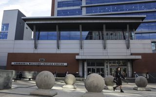 Een vrouw loopt langs een groot gebouw waar op de gevel staat dat hier het Leonard L. Williams Justice Center is gevestigd.