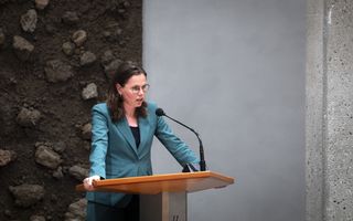 Een vrouw in een groenblauwe blazer staat achter een katheder.