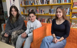 Drie leerlingen zitten in oranje stoelen in schoolbibliotheek