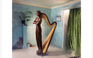 In een kamer met lichtblauwe muren en een lichtgroen gordijn staat een harp. Op de foto is voor aan de harp een staand beeld van een jongeman gemonteerd.