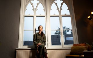 Vrouw in groene jurk zit tegen de ramen van een oud gebouw. In haar hand heeft ze een viool.