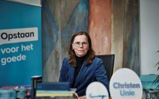 Een vrouw met een blauwe blazer zit achter een tafel waarop boeken liggen.