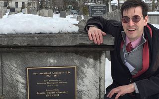 Een man staat gehurkt bij een grijze graftombe, die met sneeuw bedekt is.