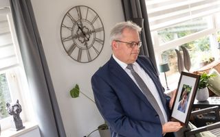 Man in pak houdt een fotolijst met een foto van zijn vrouw vast. 