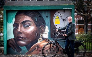 Donker geklede man met een ouderwetse fiets naast een straatschilderij van een Afrikaanse vrouw.