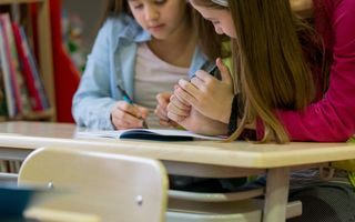 Twee schoolgaande meisjes werken samen aan een opdracht.