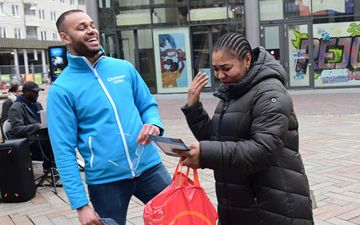 Jongeman in blauw jack lacht hard. Een donkere vrouw lacht ook en bekijkt een flyer. 