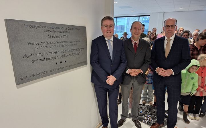 Drie mannenin pak; achter hen gezinnen met kinderen.