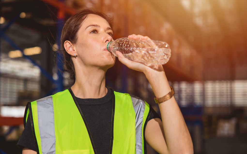 Een vrouw in een magazijn drinkt water uit een flesje. Maatregelen tegen gezondheidsklachten door hitte kunnen en mogen veel meer aandacht krijgen op de werkvloer, stelt een onderzoeker van de Vrije Universiteit. beeld iStock 