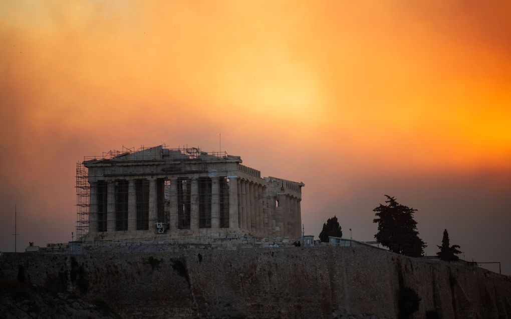 Een oranje gloed boven het Parthenon op de Akropolis in Athene. In de buitenwijken van de stad woeden bosbranden. beeld AFP, Angelos Tzortzinis.