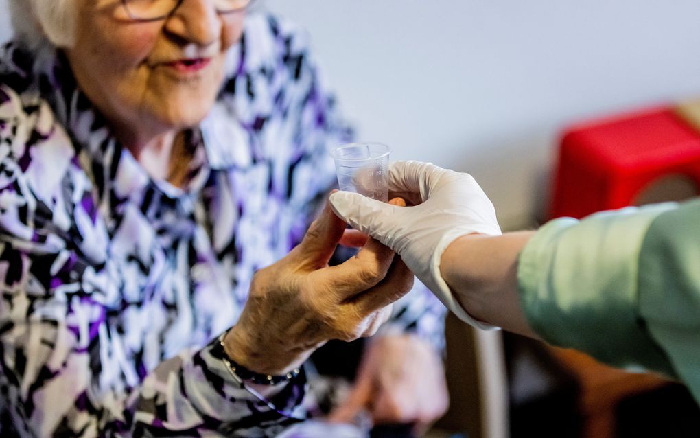 Een zorgmedewerker reikt een bewoner in een verzorgingshuis medicijnen aan. beeld ANP, Remko de Waal