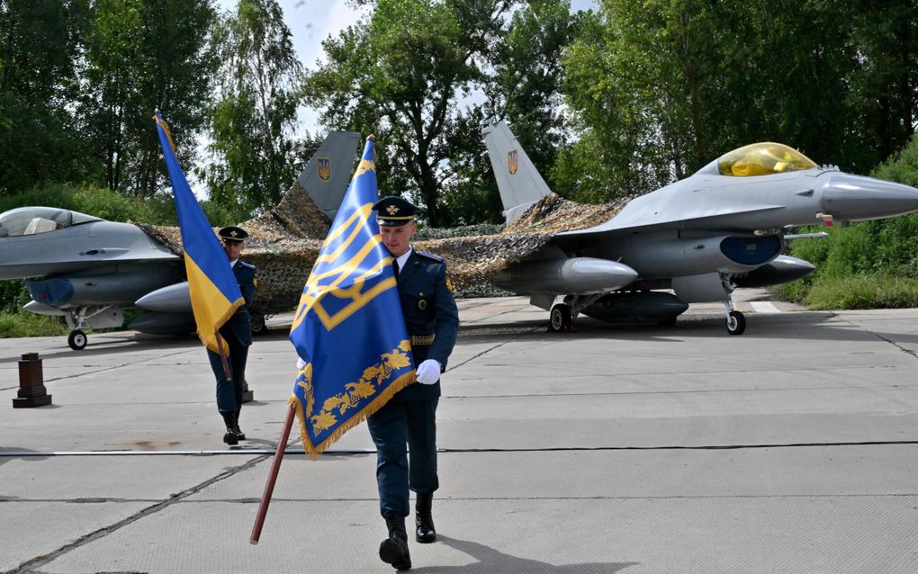 Militairen dragen een Oekraïense vlag en een vaandel tijdens de ceremoniële overdracht van westerse F-16-jachtvliegtuigen aan Oekraïne. beeld AFP, Sergei Supinsky