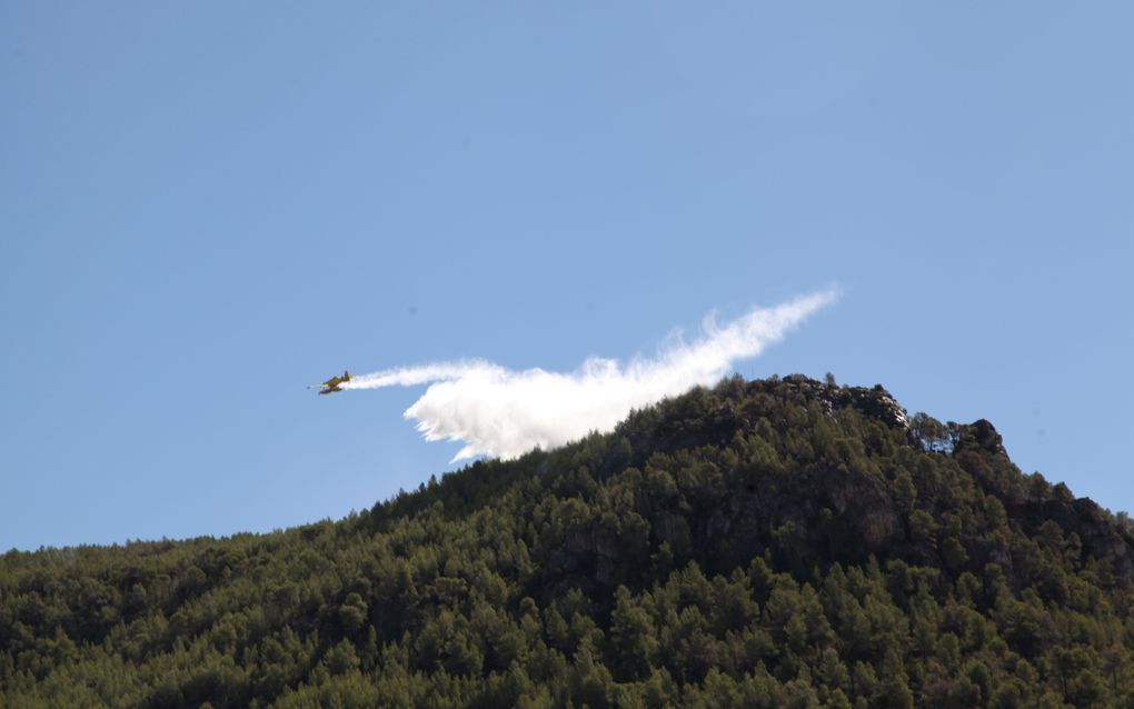 Een blusvliegtuig werpt water uit boven de heuvels nabij Cabacés. beeld Lex Rietman