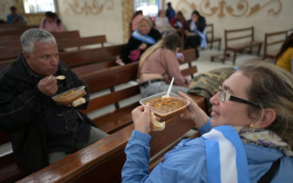 Mensen eten een gratis maaltijd in een rooms-katholieke kerk in Buenos Aires. Naast de kleine Nederlandse gereformeerde kerk in de stad verstrekken ook andere kerken voedselhulp. beeld AFP, Juan Mambromata