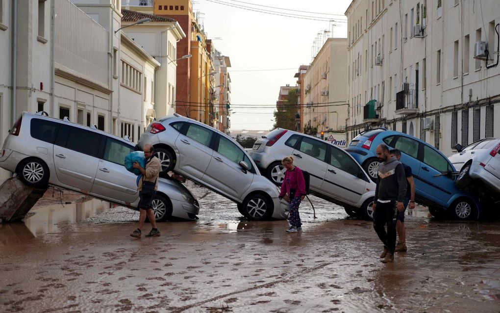 Mensen lopen in Valencia door de modder langs auto’s die door de overstromingen van dinsdag en woensdag op elkaar zijn gestapeld. beeld AFP, Manaure Quintero