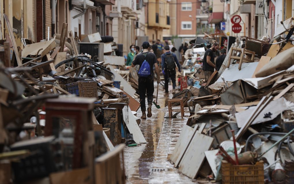 Mensen banen zich een weg door stapels huisraad die in de Spaanse stad Paiporta op straat liggen na de verwoestende waterstromen van vorige week. beeld EPA, Manuel Burque