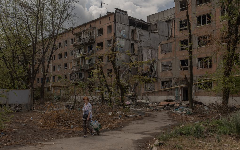 Een Oekraïense vrouw loopt langs een verwoest woongebouw na een beschieting terwijl ze lege flessen met water vult in de stad Toretsk. beeld AFP, Roman Pilipey 