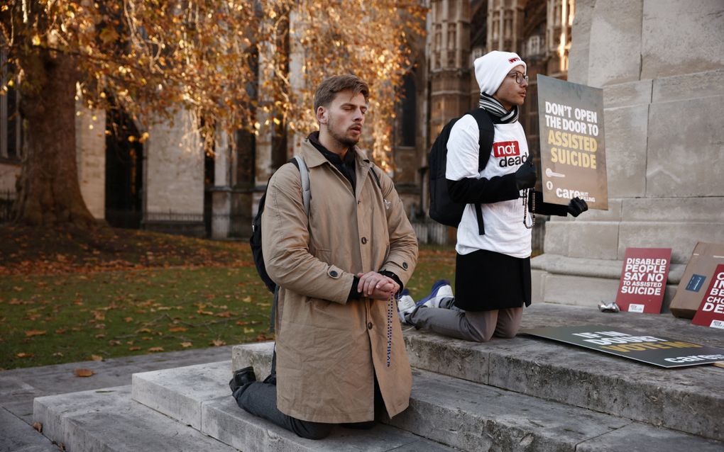 Demonstranten die tegen euthanasie zijn, bidden knielend voor het Paleis van Westminster in Londen, als eind november de wet wordt aangenomen waarmee euthanasie in het gehele Verenigd Koninkrijk wordt gelegaliseerd. beeld AFP, Benjamin Cremel