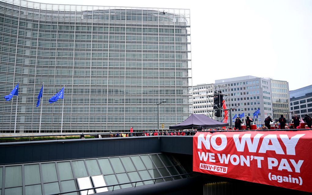 Een spandoek met de tekst ”No way, we won't pay (again)” hangt boven een tunnel die onder de Schumanrotonde doorgaat. Op de achtergrond het Berlaymontgebouw, het hoofdkwartier van de Europese Commissie in Brussel. beeld Belga, Laurie Dieffembacq