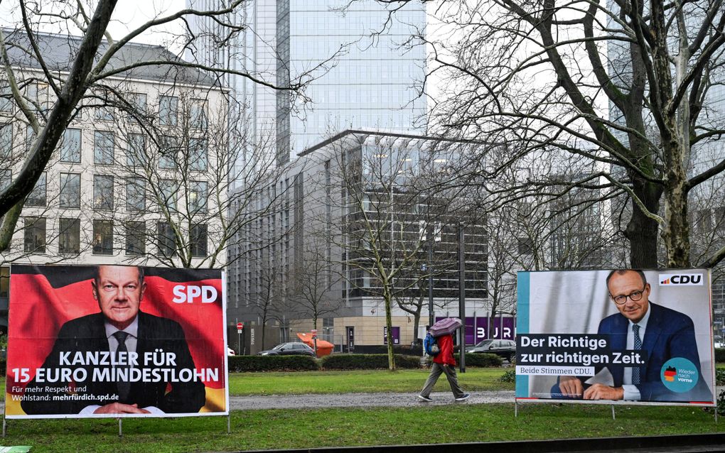 Een man loopt in Frankfurt am Main langs een verkiezingsposter met het portret van CDU-leider Friedrich Merz (r.) en het portret van de Duitse kanselier Olaf Scholz, de belangrijkste kandidaat voor de SPD. beeld AFP, Kirill Kudryatsev 