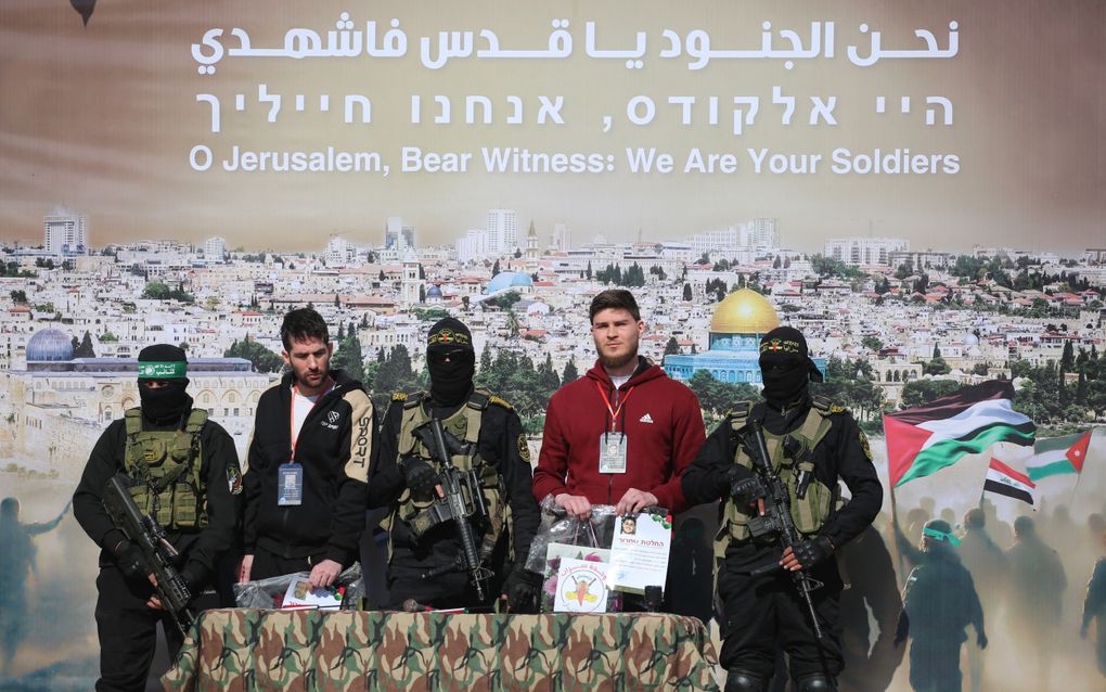 De Israëlisch-Amerikaanse Sagui Dekel-Chen en de Israëlisch-Russische Sasha Trupanov staan op het podium naast Palestijnse militanten tijdens hun overdracht aan een team van het Rode Kruis in Khan Yunis. beeld AFP, Eyad Baba