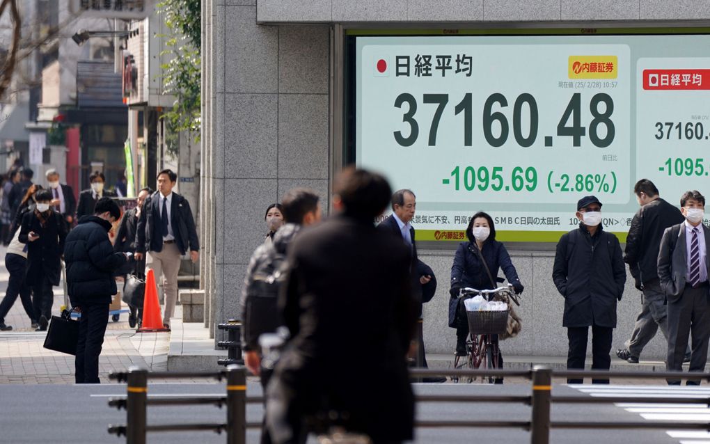 Publiek in de Japanse hoofdstad Tokio loopt vrijdag langs een bord waarop te zien is dat de Nikkei-index in het rood staat. Ook in Amerika en Europa dalen de koersen van veel aandelen uit vrees voor een handelsoorlog. beeld AFP, Kazuhiro Nogi