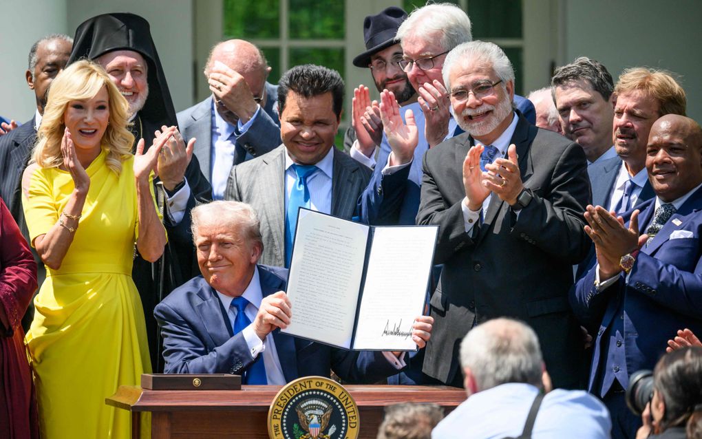 President Trump, omgeven door religieuze leiders, houdt het decreet omhoog waarmee hij de commissie godsdienstvrijheid donderdag installeerde. Links naast hem welvaartspredikster Paula White. De bijeenkomst in het Witte Huis in Washington had plaats in het kader van de Nationale Dag van Gebed. beeld AF, Mandel Ngan
