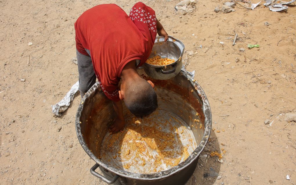 Een Palestijnse jongen schraapt de laatste restjes uit een gamel tijdens een voedseluitdeling in de stad Gaza, maandag. beeld AFP, Omar Al-Qattaa