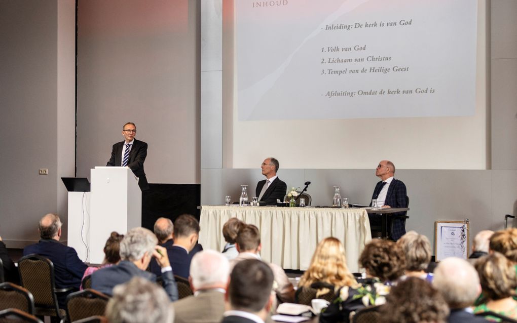 Ds. M.K. de Wilde houdt een inleiding op de jaarvergadering van de Gereformeerde Bond. Op het podium zitten voorzitter ds. J.A.W. Verhoeven (l.) en algemeen secretaris P.J. Vergunst, die benoemd werd als erelid. beeld André Dorst