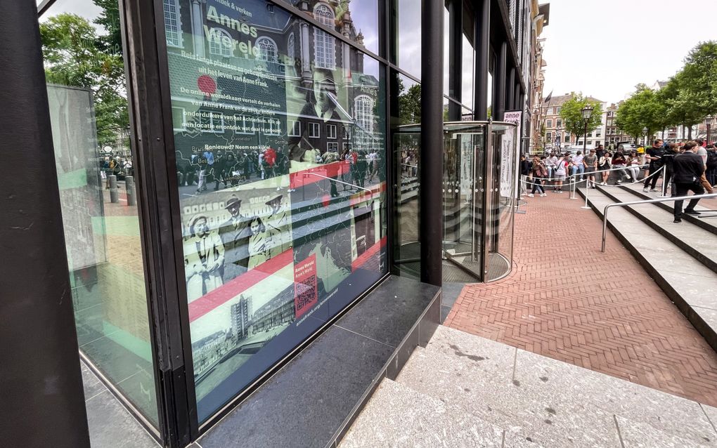 Ingang van het Anne Frank Huis, met grote groep wachtende bezoekers bij de deur. Op de voorgrond een affiche met ”Annes Wereld”.