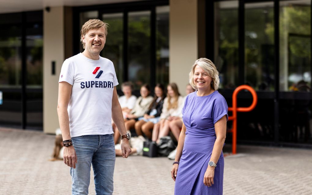 Een man met een wit T-shirt en een spijkerbroek en een vrouw met een paarse jurk staan voor de hoofdingang van de Pieter Zandt scholengemeenschap.
