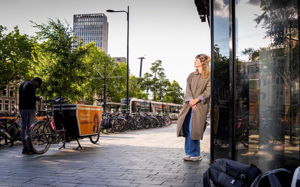 Vrouw in lange, bruine jas staat bij de ingang van de Pauluskerk, waarnaast een stapel jassen en koffers ligt.