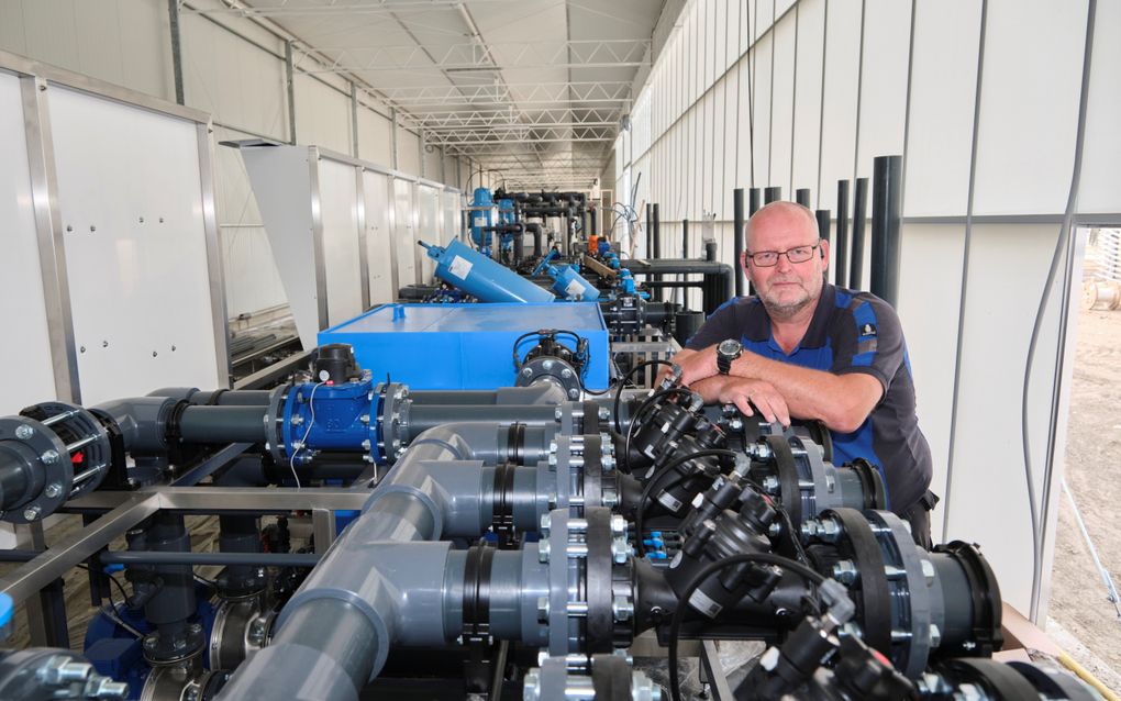 Een man met bril leunt op een installatie met allerlei buizen en slangen. 