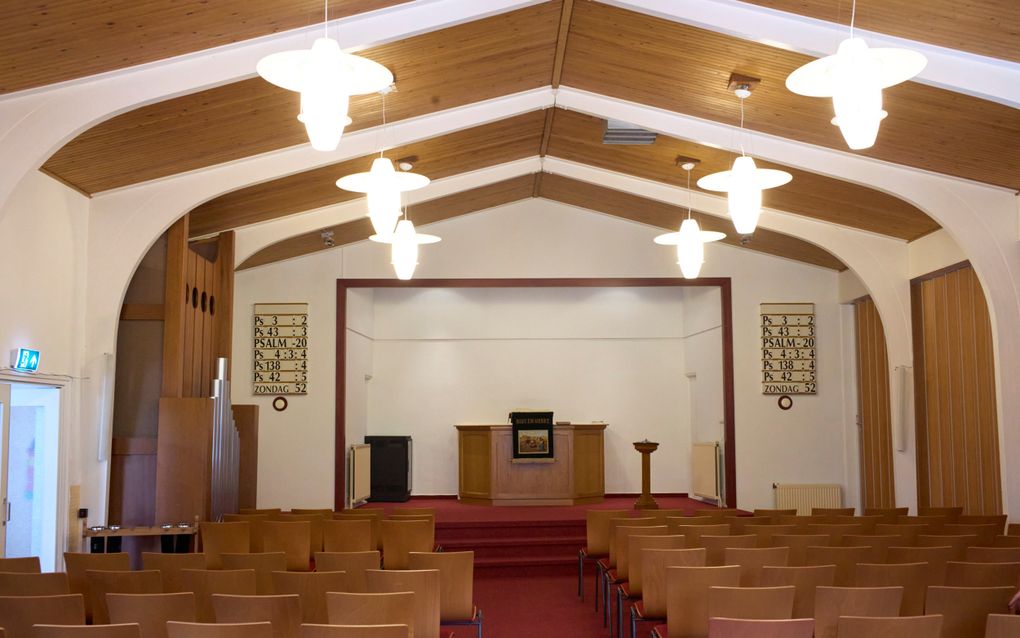 Een kerkzaal met houten stoelen en rode vloerbedekking; links een klein pijporgel, in het midden een kansel. Voorin hangen psalmborden