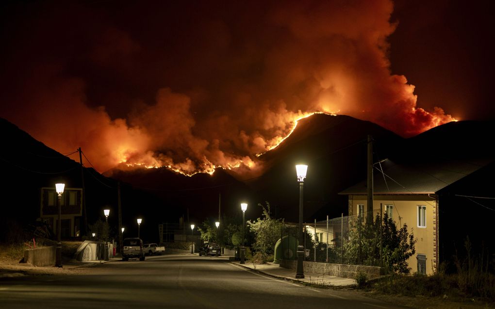 Uitgestorven dorpje met brandende lantaarnpalen. Op de achtergrond bergen met vlammen. 
