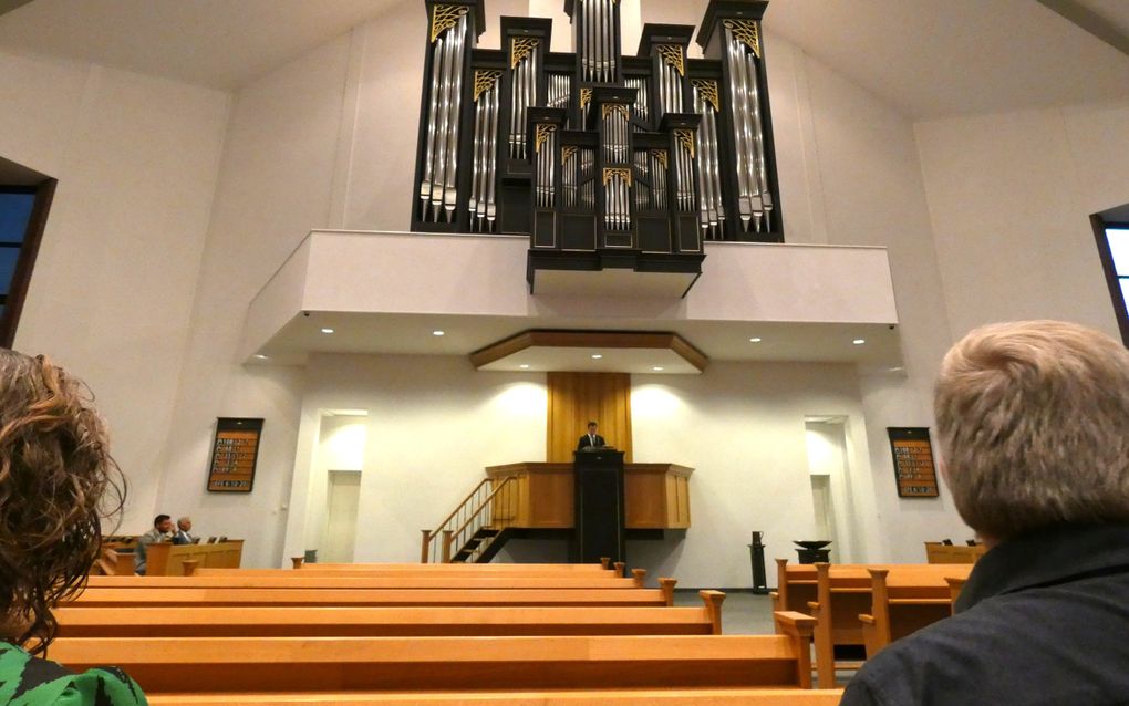 Kerk met groot orgel en predikant op de kansel. Op de voorgrond twee mensen.