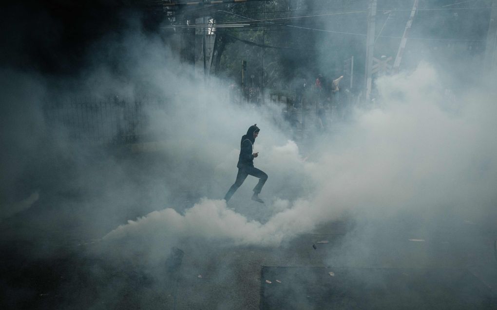 Een donkergeklede man rent door een mist van traangas. 