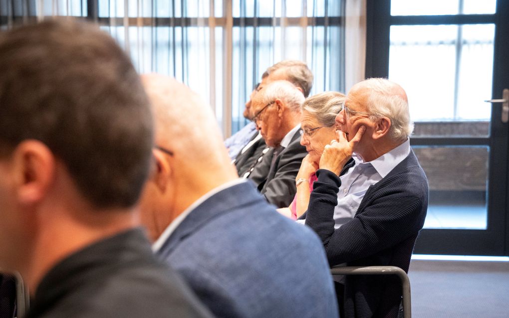 Mensen luisteren in een zaal naar een spreker.